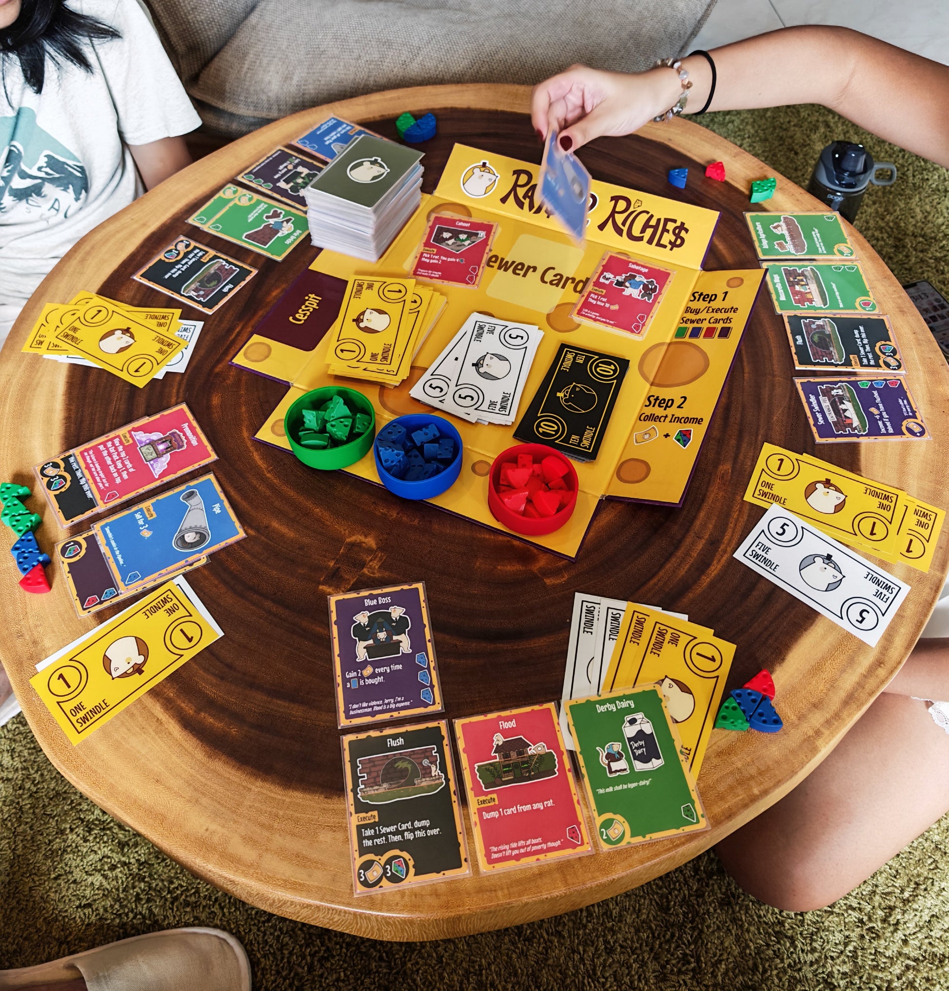 People playing a card game around a wooden table with colorful cards and game pieces.
